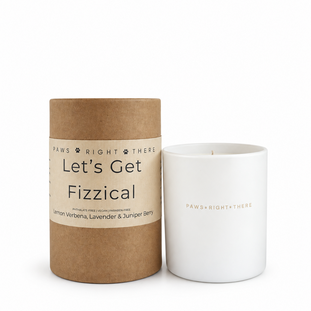 A white ceramic candle jar next to its brown kraft paper cylindrical packaging tube. The tube features a white paper label with the text 'PAWS RIGHT THERE Let's Get Fizzical'.
